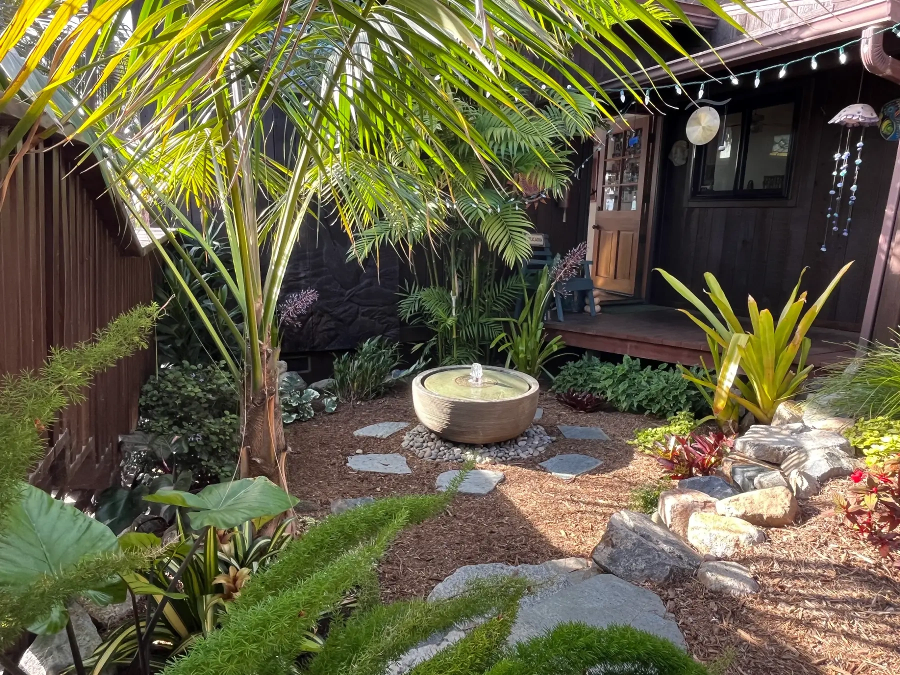 Front view of Leucadia backyard featuring lush planting enhancement, stone water feature, and natural flagstone pathway.