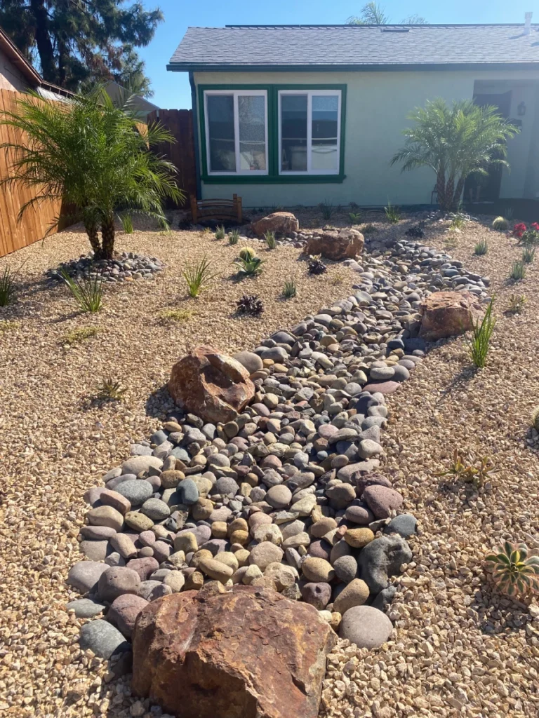 Front view of decomposed granite, dried creek bed, and prefab wood bridge in outdoor renovation.